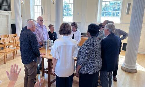 A group of faculty and staff gather around a round table for blessing and rededication.